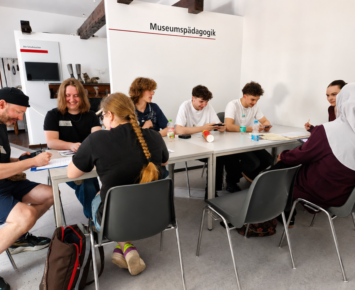 Jugendliche arbeiten im Workshop an Tischen in einem Museumsraum