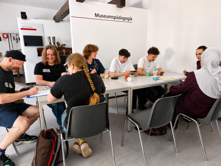 Jugendliche arbeiten im Workshop an Tischen in einem Museumsraum