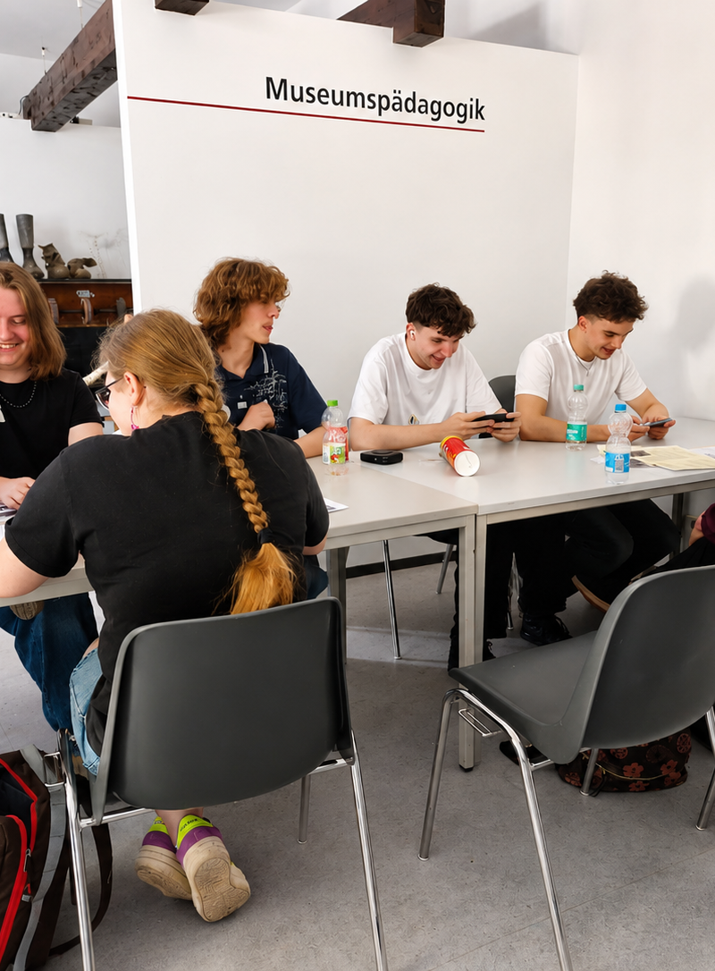 Jugendliche arbeiten im Workshop an Tischen in einem Museumsraum